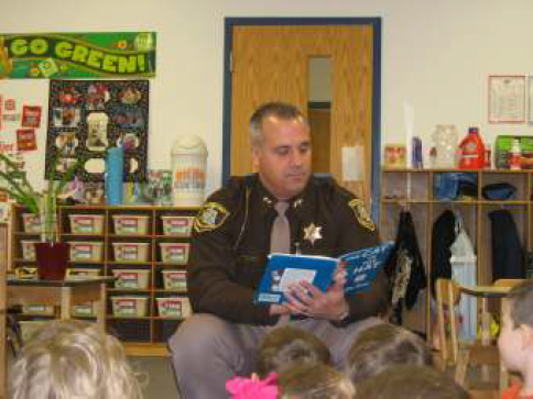 Sheriff reading "The Cat in the Hat" to students sitting on floor.