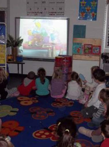 Students sitting in circle on floor looking up at smart board